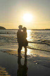 Young couple kissing each other in front of sea on beach at sunset - SSGF00771