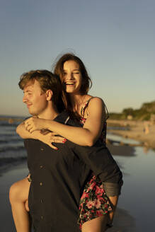 Mann nimmt Frau am Strand bei Sonnenuntergang huckepack - SSGF00773