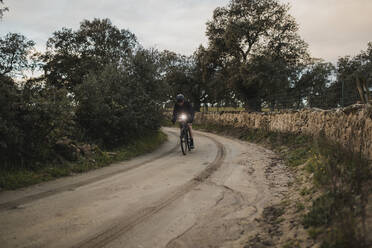 Mann fährt Fahrrad auf der Straße bei Sonnenaufgang - DMGF00688