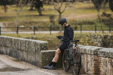 Cyclist using mobile phone leaning on wall - DMGF00712