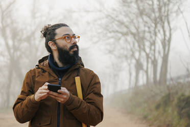 Älterer Mann mit Brille und Smartphone, verloren im Wald - MRRF02004