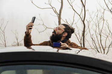 Älterer bärtiger Mann, der hinter einem Auto stehend sein Smartphone überprüft - MRRF02009