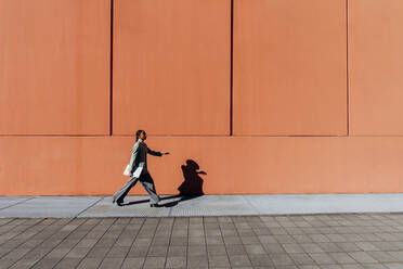 Businesswoman with laptop walking by orange wall - MEUF05175