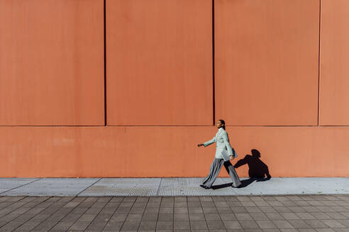 Young businesswoman with laptop walking by orange wall - MEUF05176