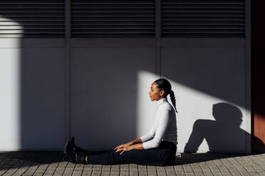 Junge Geschäftsfrau sitzt an der Mauer auf dem Fußweg - MEUF05192