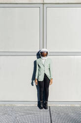 Businesswoman wearing space helmet in front of wall - MEUF05200