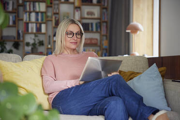 Lächelnde Frau mit Tablet-PC auf dem Sofa zu Hause - RBF08881