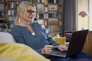 Lächelnde Frau mit Kreditkarte und Laptop auf dem Sofa zu Hause - RBF08884