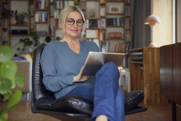 Smiling woman with tablet PC sitting on chair at home - RBF08888