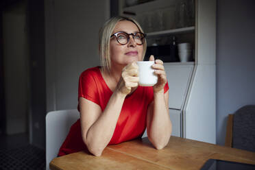 Nachdenkliche Frau mit Teetasse am Tisch sitzend - RBF08894