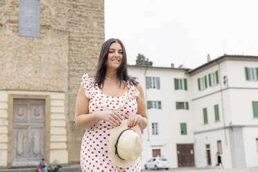 Lächelnde Frau in gepunktetem Kleid vor einem Gebäude stehend - EIF03931
