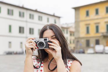 Happy woman taking picture through camera in front of buildings - EIF03935