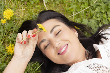Happy woman with yellow flower lying on grass - EIF03957