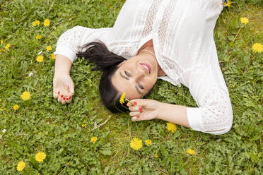 Happy woman with yellow flower lying on grass at park - EIF03958
