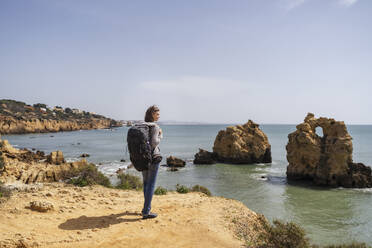 Woman with backpack looking at view standing in front of sea on sunny day - DIGF17826