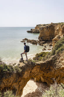 Mann mit Rucksack auf einer Felsbrücke vor dem Meer stehend - DIGF17837