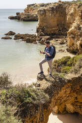 Man using smart phone standing on rock bridge - DIGF17839