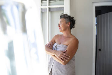 Smiling woman wearing towel standing with arms crossed at home - ESTF00026