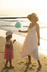 Glückliche Mutter gibt ihrer Tochter am Strand Zuckerwatte - SSGF00792