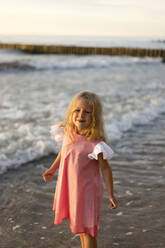 Lächelndes süßes Mädchen mit blondem Haar am Strand stehend - SSGF00801