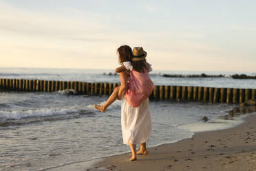 Mother giving piggyback ride to daughter at beach - SSGF00806