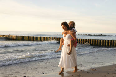 Glückliche Mutter, die ihre Tochter am Strand huckepack nimmt - SSGF00807