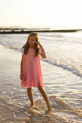 Smiling girl standing in front of sea at beach - SSGF00813