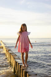 Niedliches Mädchen, das auf einem Holzpfosten am Strand spaziert - SSGF00816
