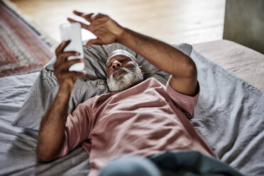 Mann mit Handy auf dem Bett liegend zu Hause - FMKF07397