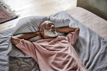 Kahlköpfiger Mann mit geschlossenen Augen ruht sich zu Hause auf dem Bett aus - FMKF07400