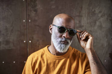 Bald man wearing sunglasses standing in front of wall stock photo