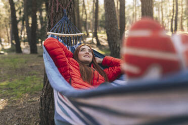 Smiling young woman with hands behind head lying in hammock - JCCMF06104