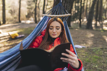 Young woman reading diary relaxing in hammock - JCCMF06105