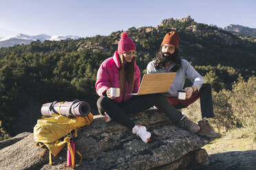 Junge Frau mit Laptop und Freund auf einem Felsen sitzend - JCCMF06108