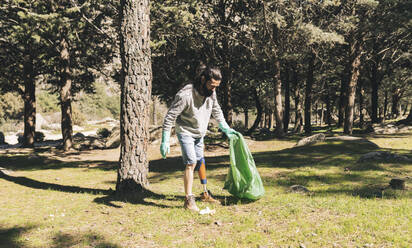 Disabled man with garbage bag in forest on sunny day - JCCMF06129