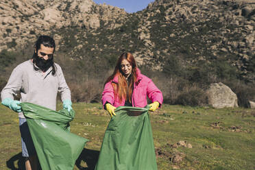 Smiling man and woman with plastic bags standing on sunny day - JCCMF06135