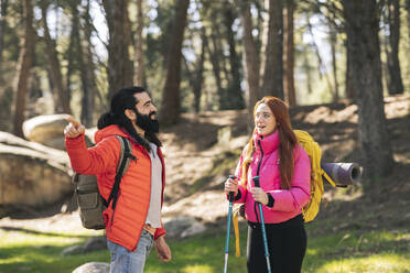 Junge Frau im Gespräch mit ihrem Freund, der einen Rucksack trägt und in den Wald zeigt - JCCMF06141