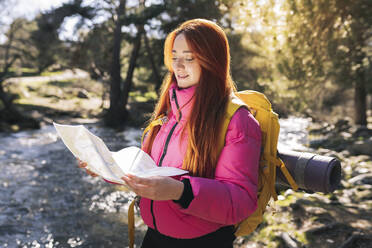 Lächelnde Frau mit Rucksack, die im Wald stehend eine Karte liest - JCCMF06145