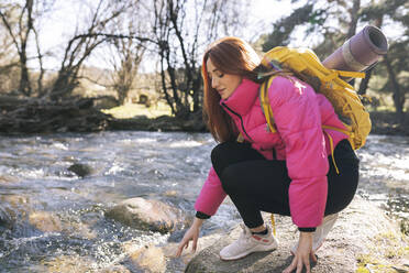 Junge Frau hockt auf einem Felsen am Fluss im Wald - JCCMF06146