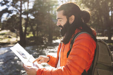 Bärtiger Mann mit Rucksack liest Karte im Wald - JCCMF06149