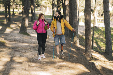 Smiling disabled man trekking with girlfriend in forest - JCCMF06169