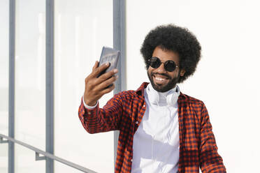 Happy man wearing sunglasses taking selfie through smart phone - MMPF00025