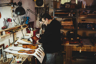 Luthier examining plans for the varnished violin on paper and on - CAVF96203