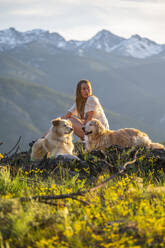 Frau in einem Kleid posiert mit Hunden mit Blick auf die Berge - CAVF96214