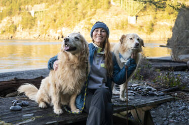 Frau sitzt auf einem Picknicktisch mit Hunden im Deception Pass State Park - CAVF96219