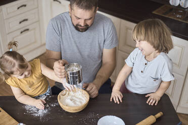 Father and children sifting flour for dough - CAVF96230