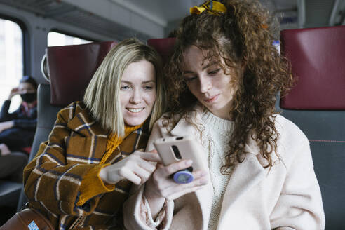 Zwei Frauen im Zug schauen auf das Telefon - CAVF96274