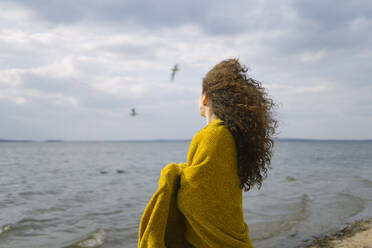 A woman stands on the shore of the lake covered with a yellow cape - CAVF96275