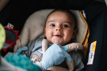 Ein Baby liegt im Kinderwagen und lächelt neben seinem Teddybär. - CAVF96277