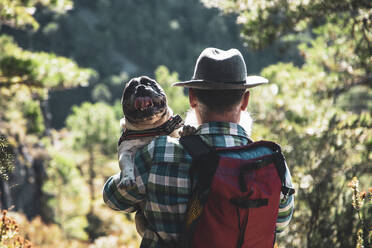 Der Bärtige geht in der Natur spazieren und trägt seinen Hund auf den Schultern. - CAVF96281